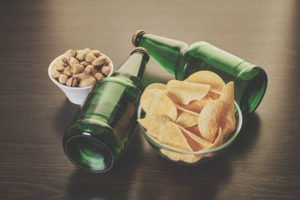 Photo of bottles of beer, potato chips, and nuts on a table.