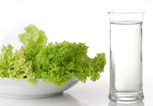 A glass of water and a bowl of lettuce